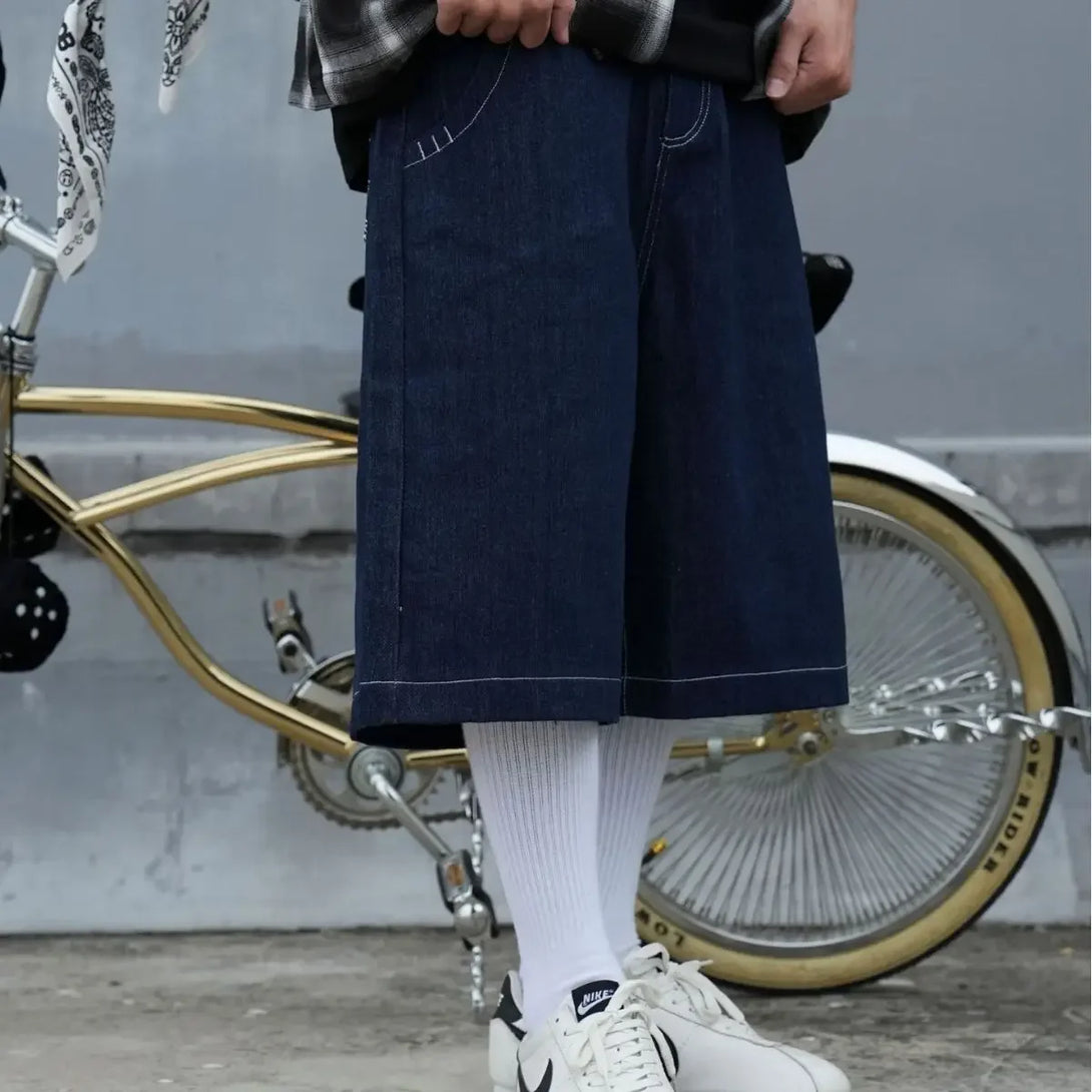 A model wearing the blue Embroidery Pockets Oversized Jorts in a gray background 